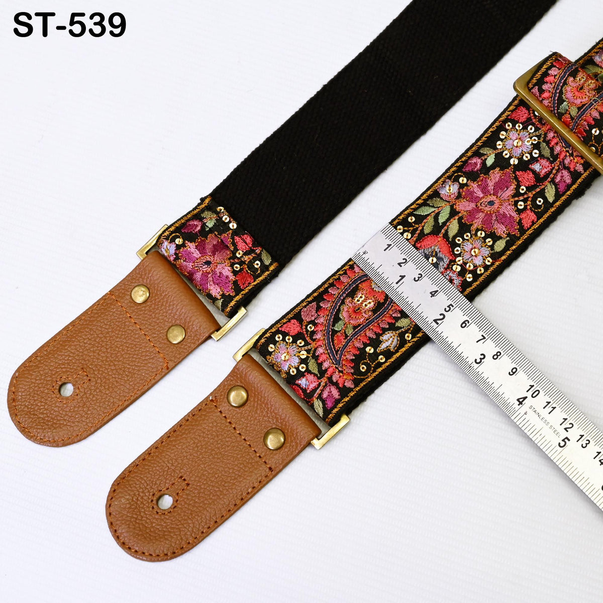 A black and brown guitar strap with a floral pattern, and a ruler placed next to it, indicating the strap's length.