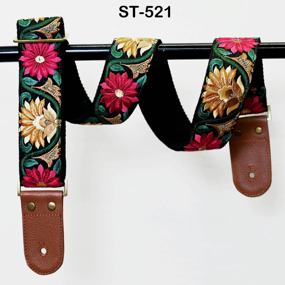 A colorful guitar strap with floral patterns, hanging on a black metal bar.