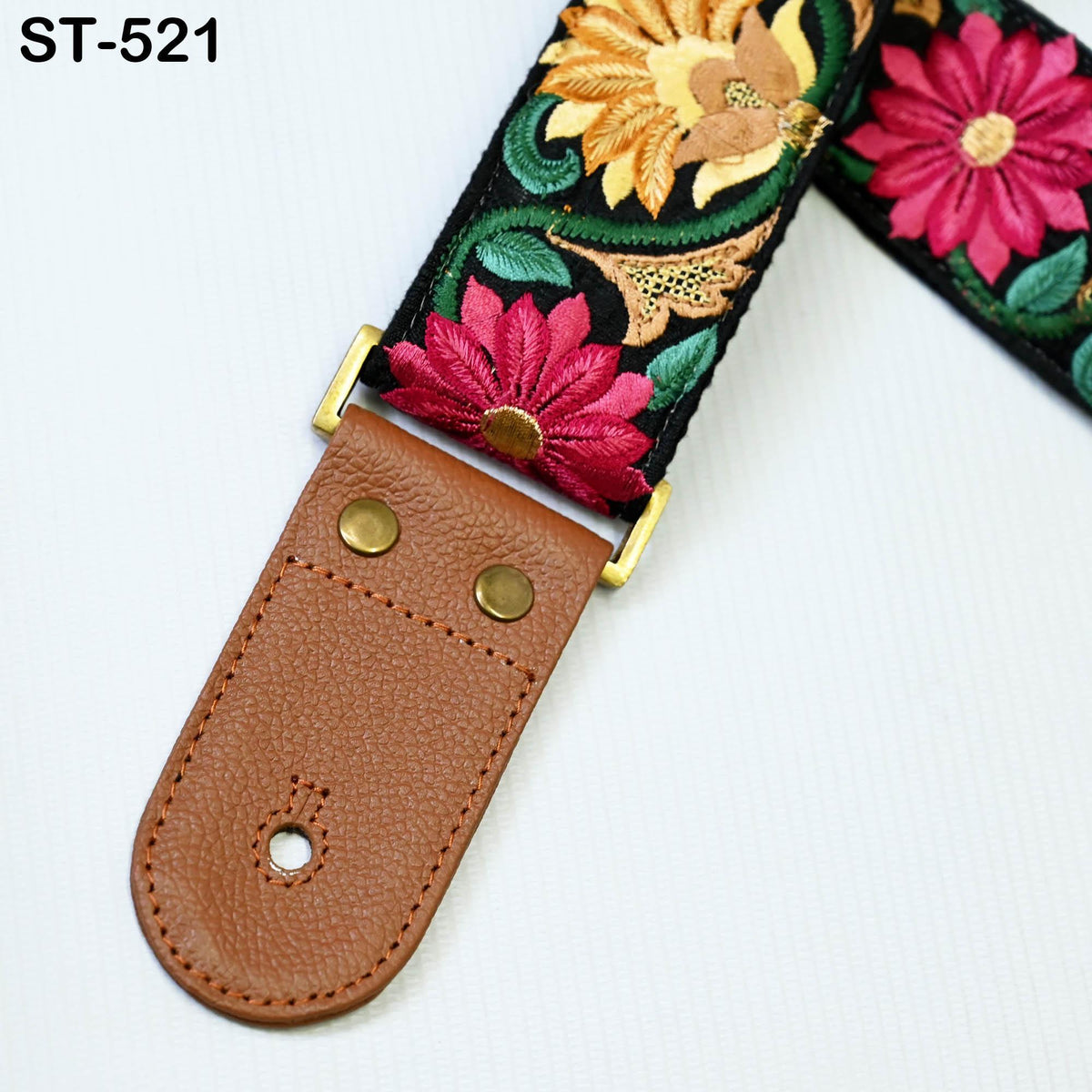 A colorful, embroidered guitar strap with a brown leather buckle.