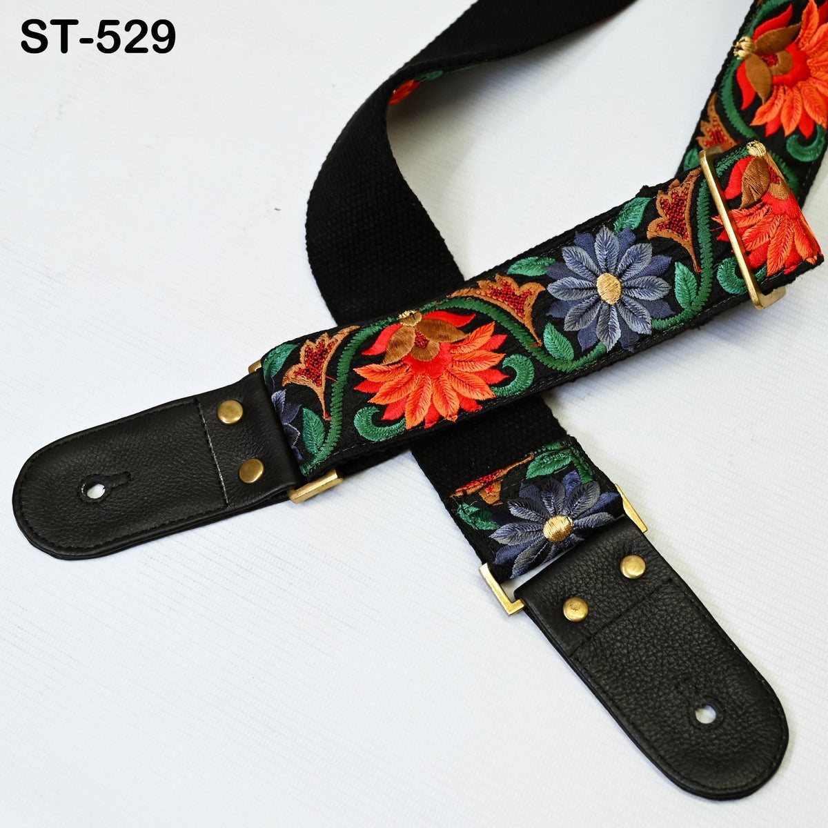 A colorful guitar strap with a floral pattern, featuring red, orange, blue, and green flowers, is shown against a white background.