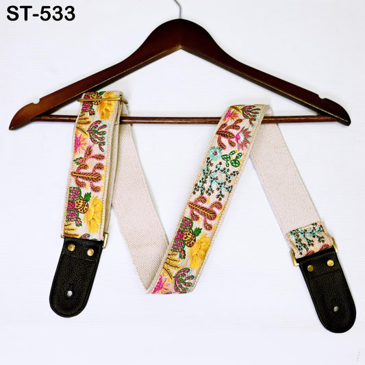A colorful, patterned guitar strap is hanging on a wooden hanger against a white background.