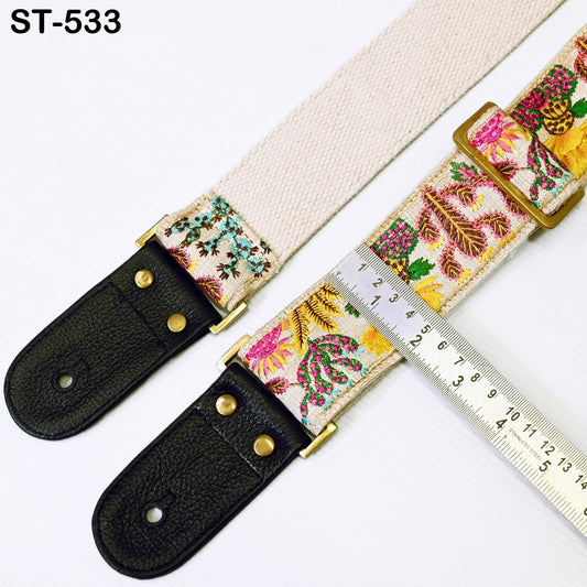 a beige guitar strap with a floral pattern, placed on a white surface next to a ruler for size comparison.