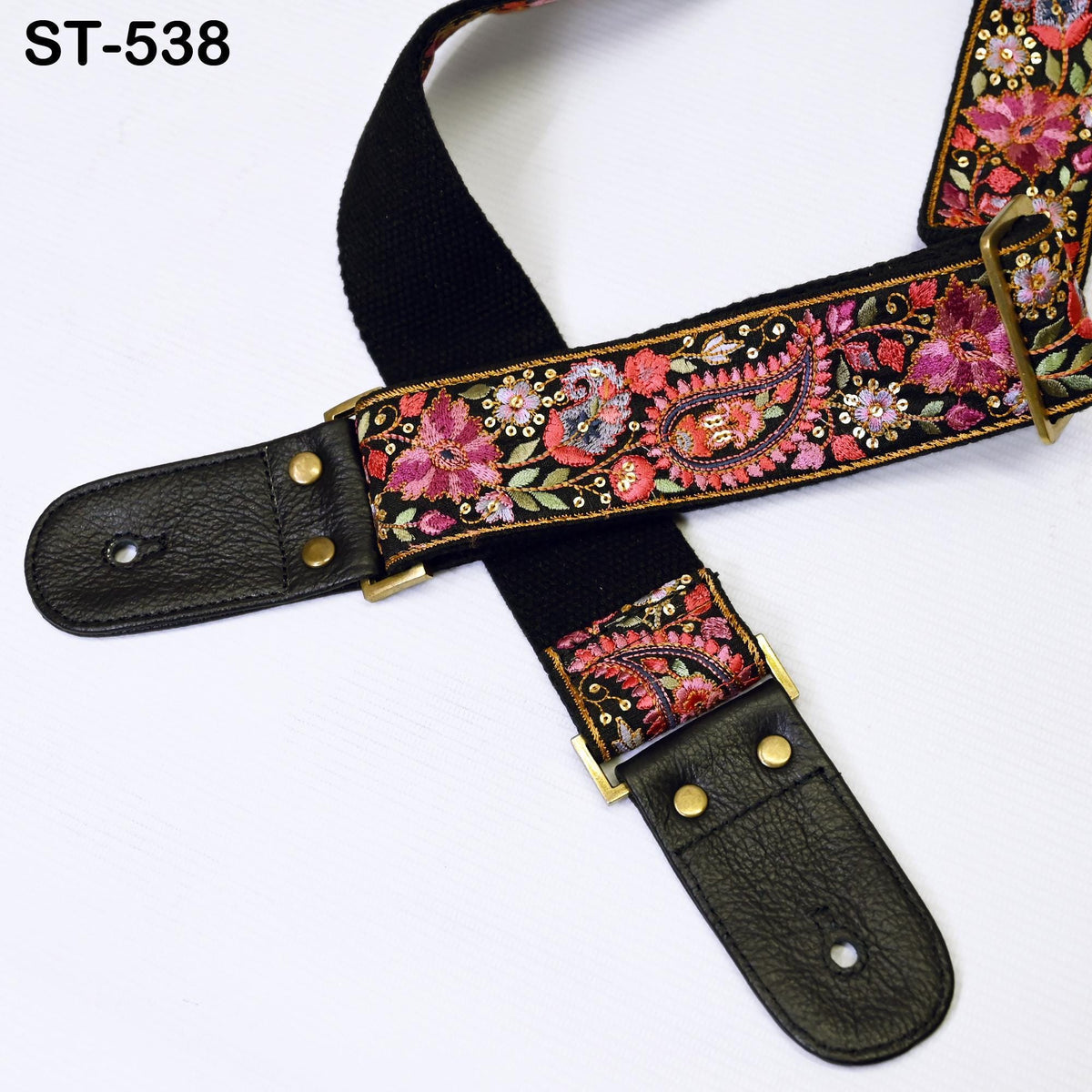 A black guitar strap with a floral pattern and gold hardware, including buckles and clips, is shown against a white background.