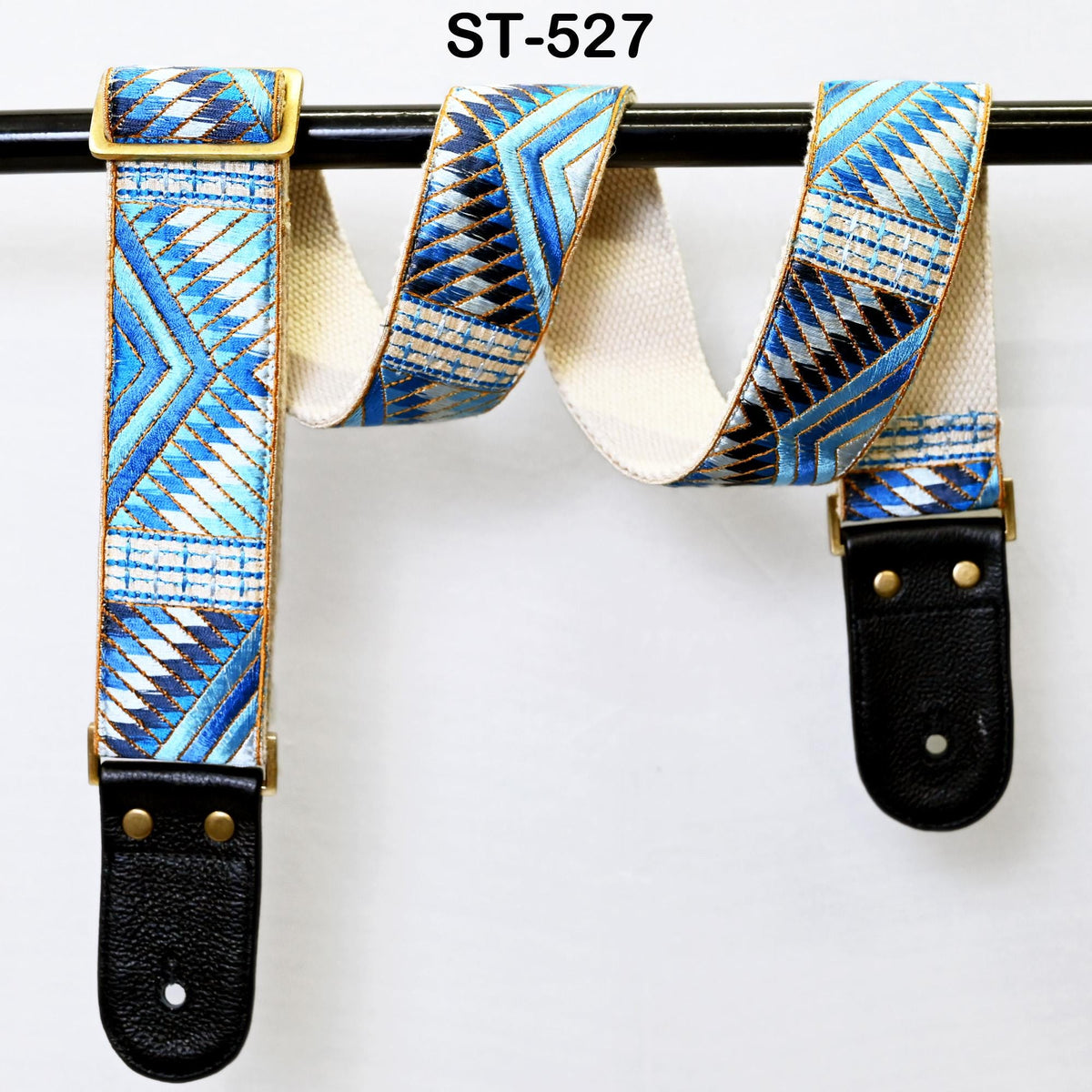 A pair of guitar straps with a geometric pattern in blue, white, and black colors, hanging on a black metal bar.