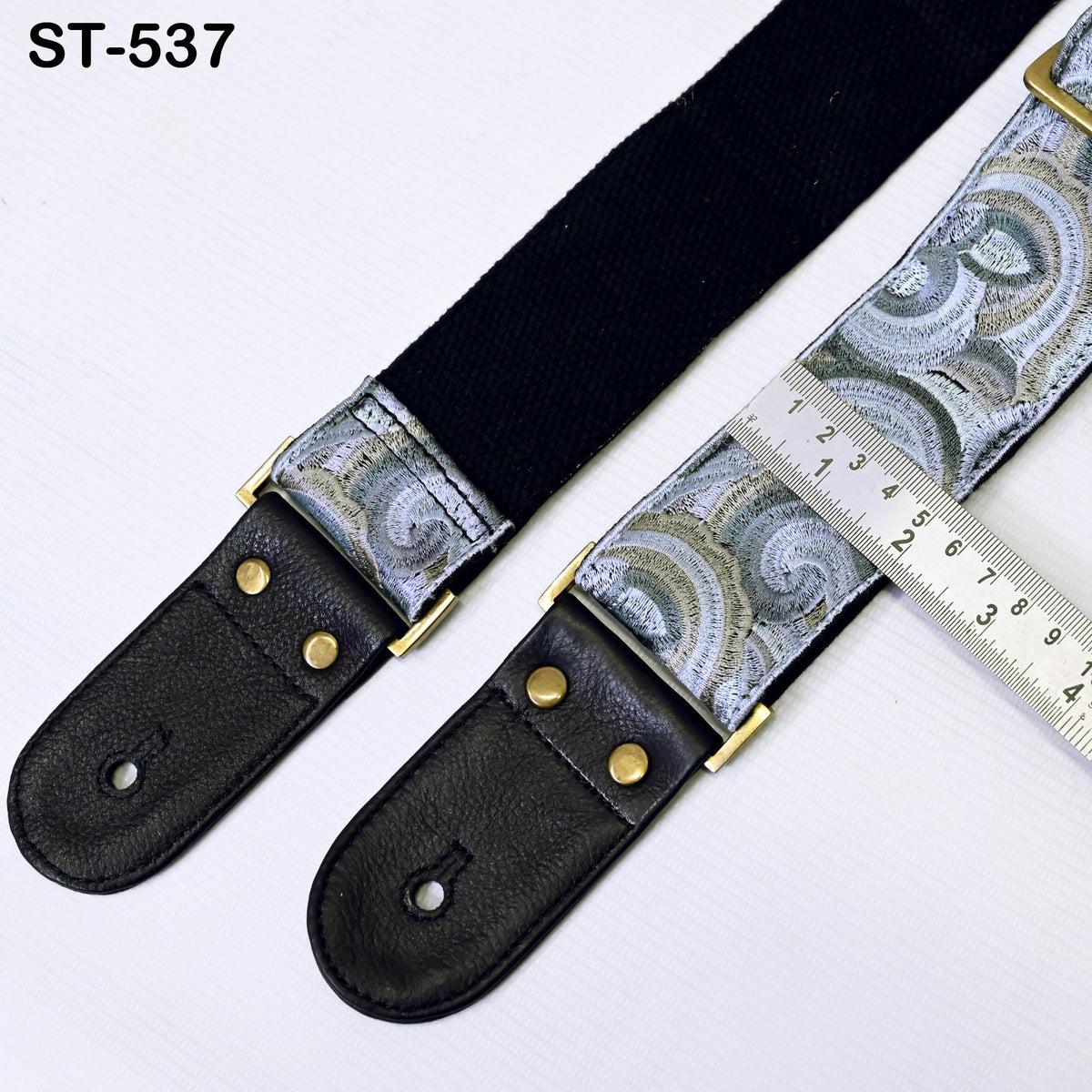 A black and silver patterned guitar strap with a ruler placed on top of it, indicating the size of the strap.
