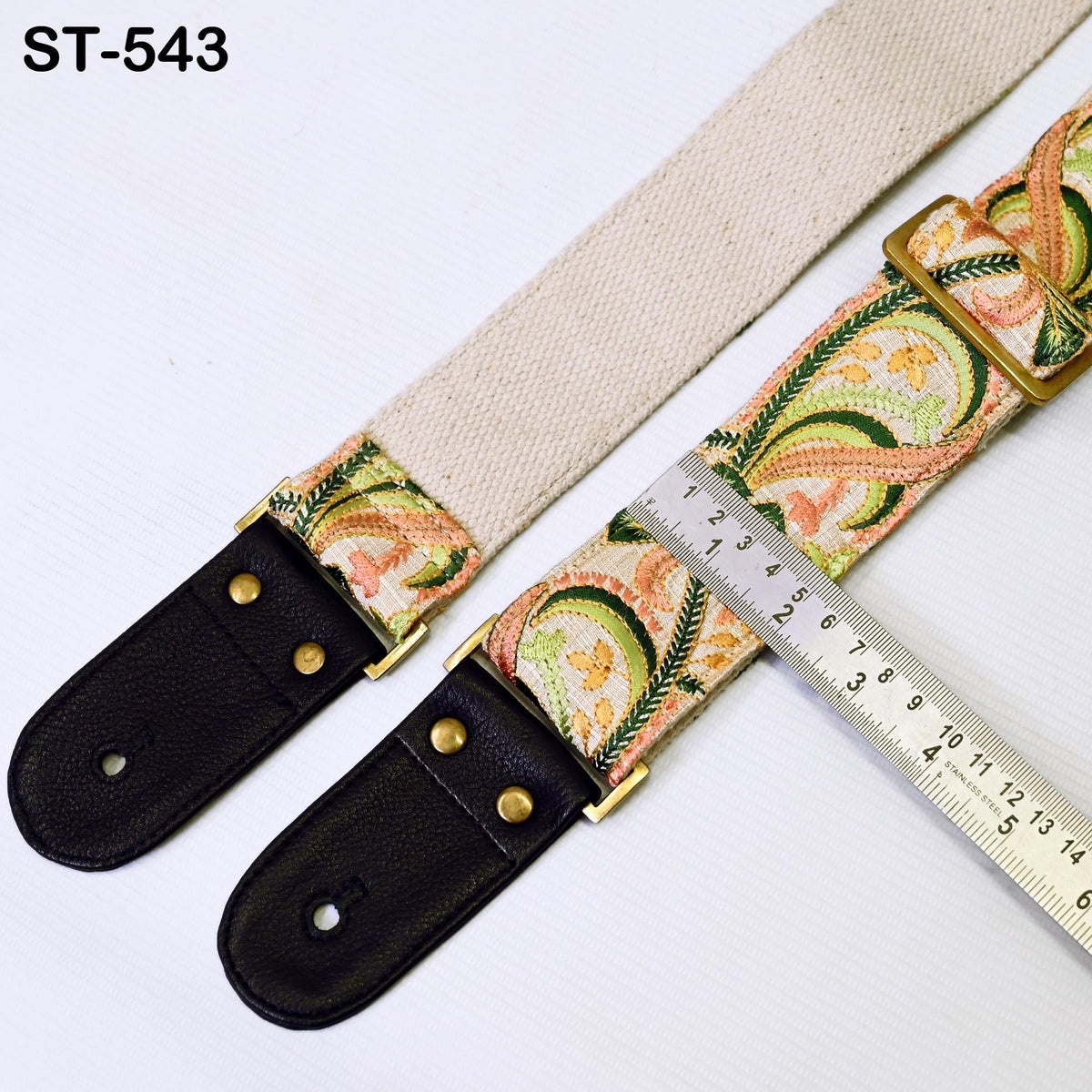 a beige guitar strap with a floral pattern and a black leather guitar pickguard. The strap is placed next to a ruler, which is used to measure the strap's length.