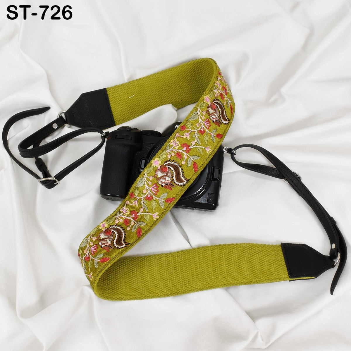 A camera strap with a floral pattern and a black camera attached to it, both resting on a white surface.