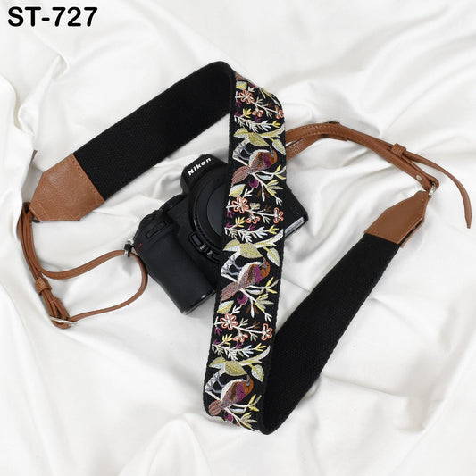 A black camera strap with a floral pattern and a black camera body are placed on a white surface.