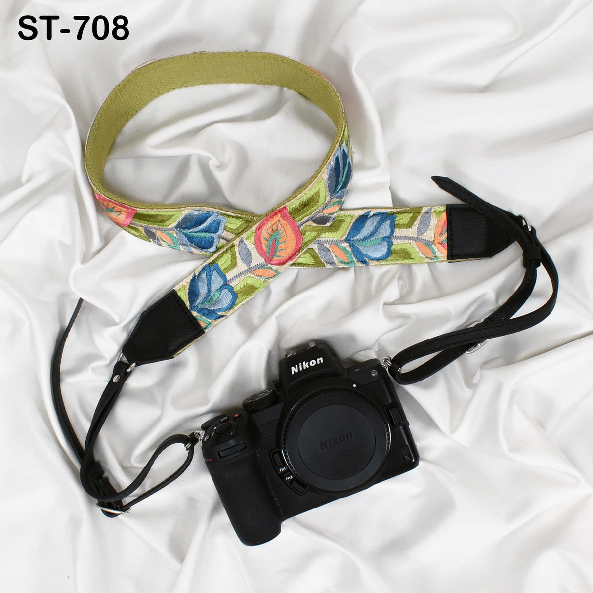 A black camera with a colorful floral patterned strap is placed on a white surface.