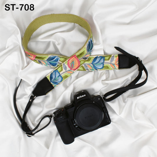 A black camera with a colorful floral patterned strap is placed on a white surface.