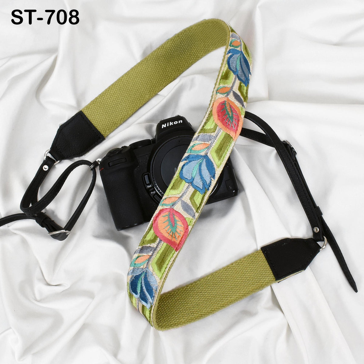 A black camera with a colorful floral patterned strap is placed on a white surface.