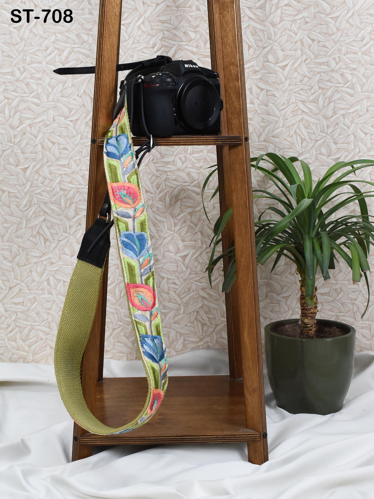 a wooden shelf with a camera strap hanging on it, and a potted plant next to the shelf.