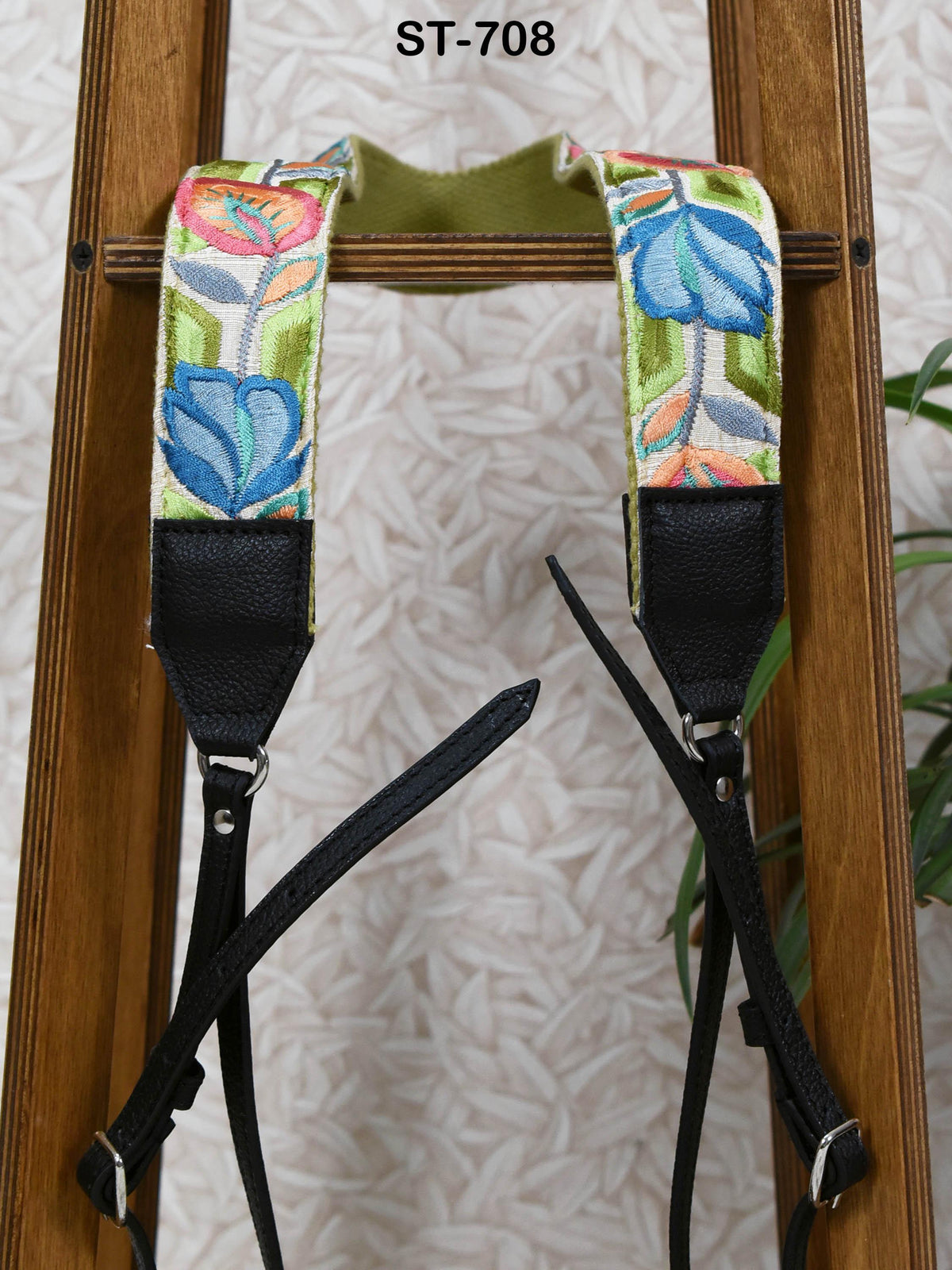 A pair of colorful floral-patterned camera straps with black leather straps, hanging on a wooden stand.