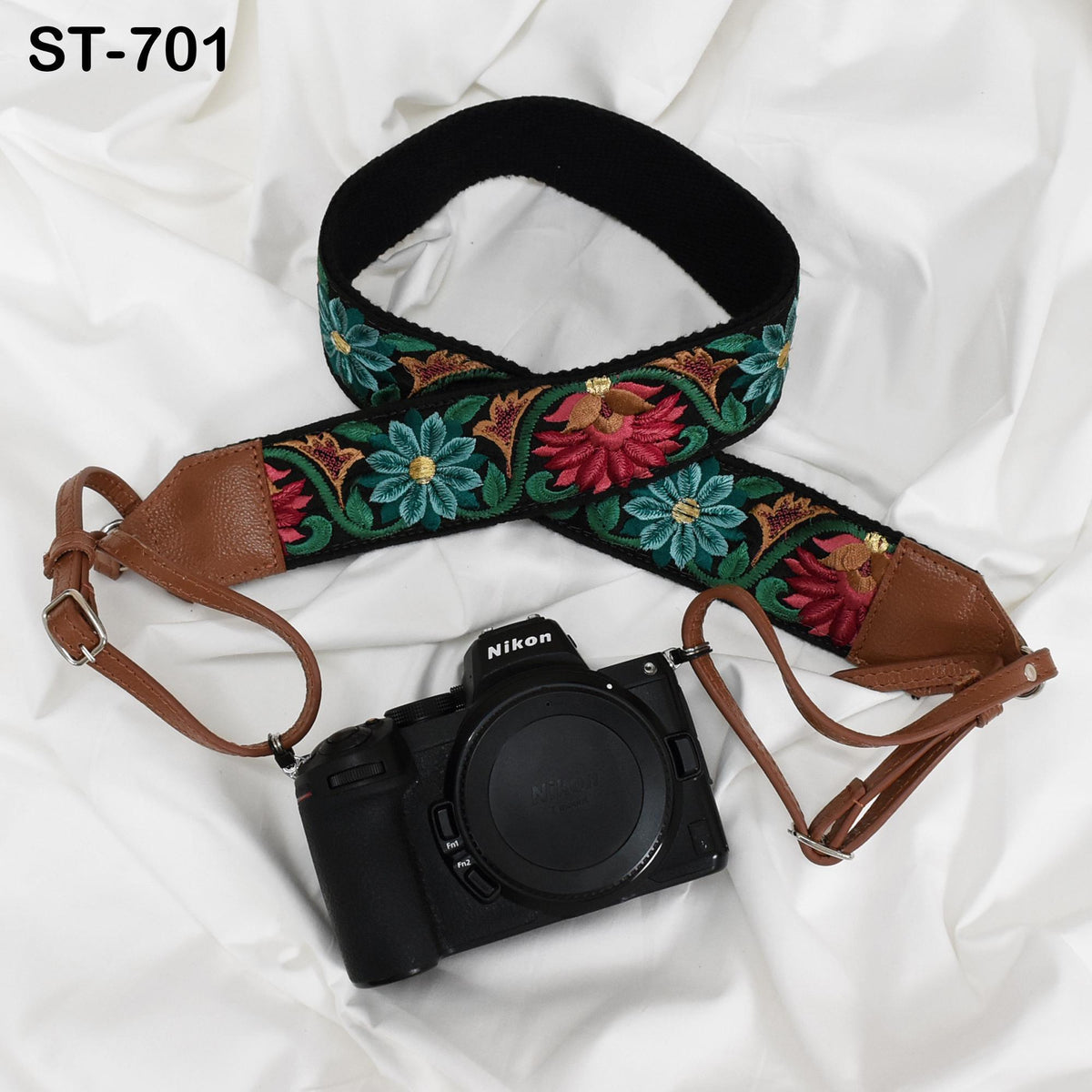 A black camera with a floral patterned strap and a black strap are placed on a white background.