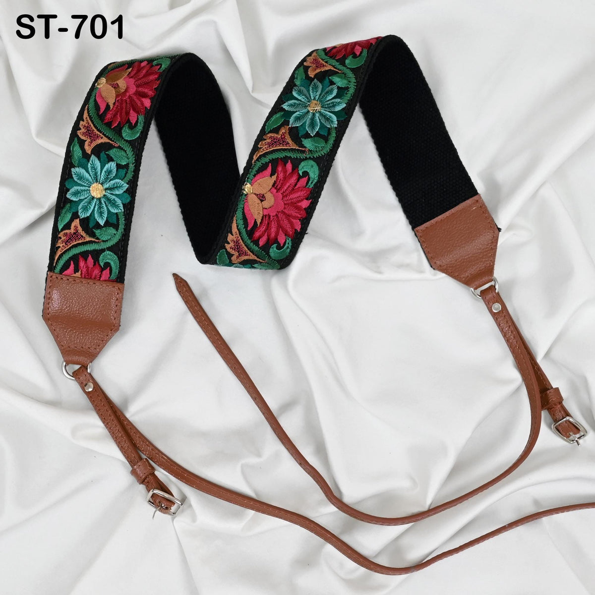 A brown leather strap with a floral embroidered pattern on it, resting on a white fabric surface.