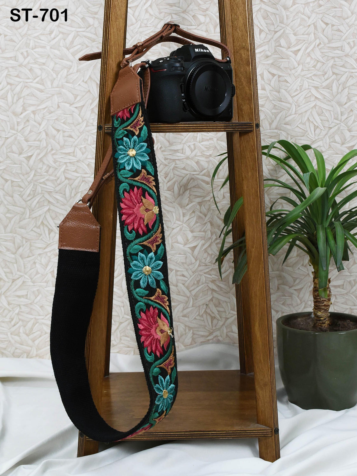 a camera strap with a floral pattern hanging on a wooden stand, accompanied by a black camera on the stand.