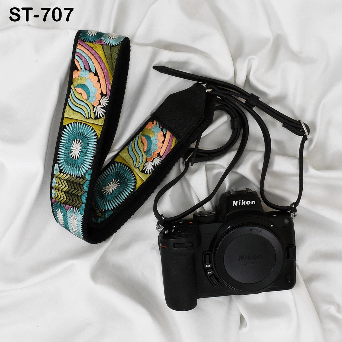 A black camera with a colorful patterned strap and a black strap are placed on a white surface.
