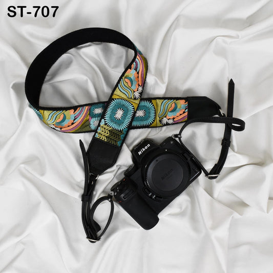 A colorful patterned camera strap and a Nikon camera are placed on a white fabric surface.