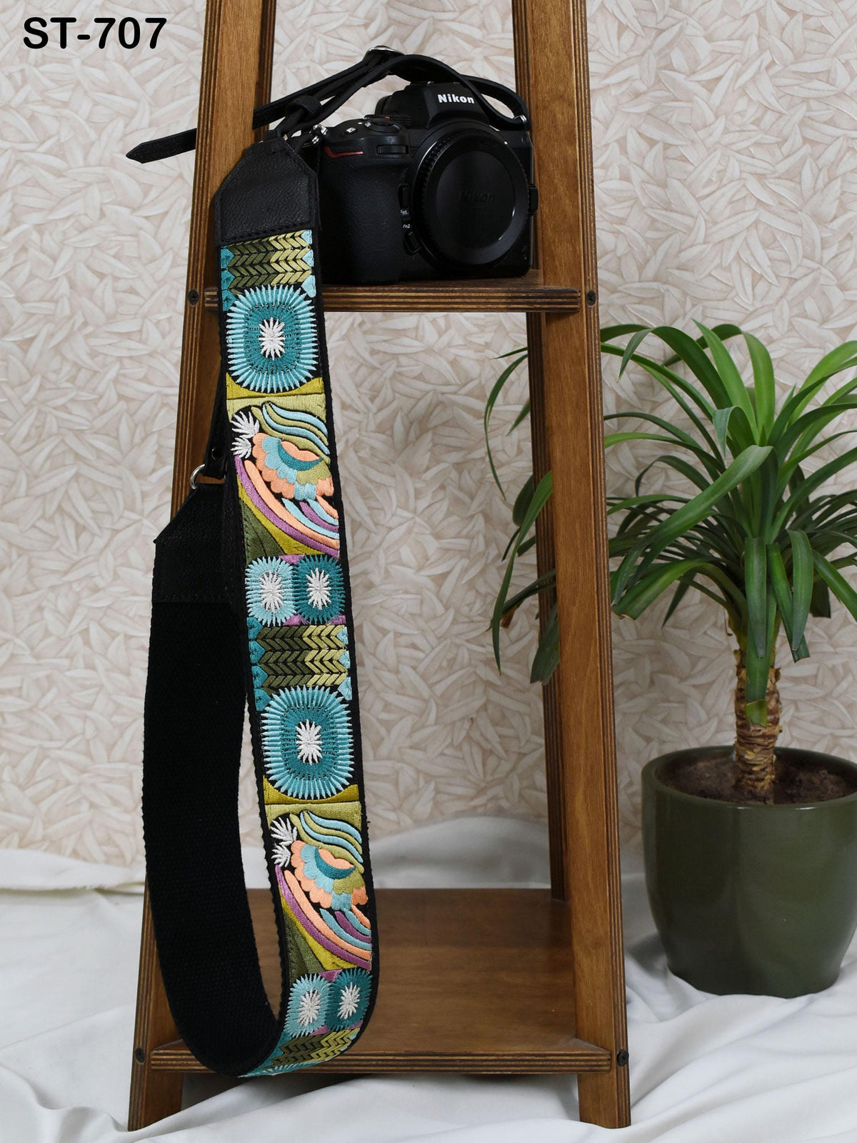 a wooden shelf with a black camera strap hanging on it, and a potted plant next to the shelf.