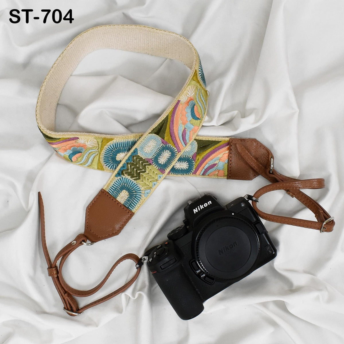 A colorful patterned camera strap and a black Nikon camera are placed on a white fabric surface.