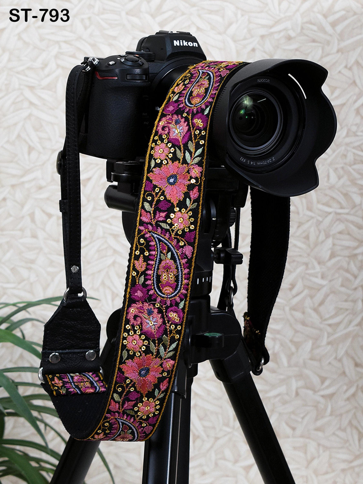 A black camera with a colorful floral patterned strap is mounted on a tripod, with a blurred background.
