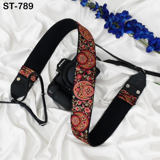 A black camera strap with a colorful floral pattern is placed next to a bouquet of blue flowers on a white surface.