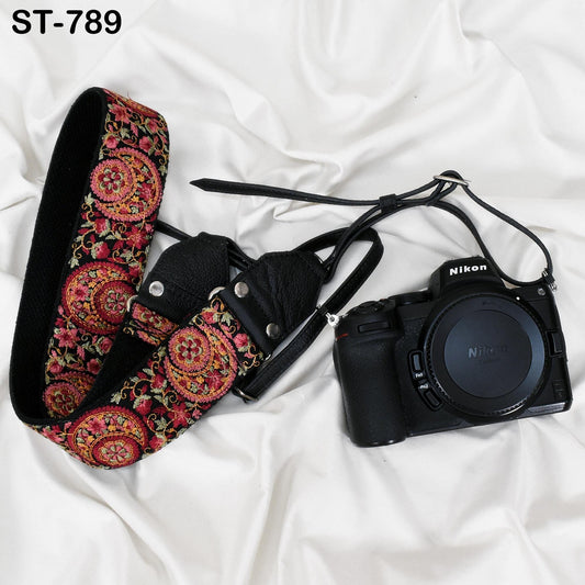 A black and pink patterned camera strap and a black Nikon camera are placed on a white surface.