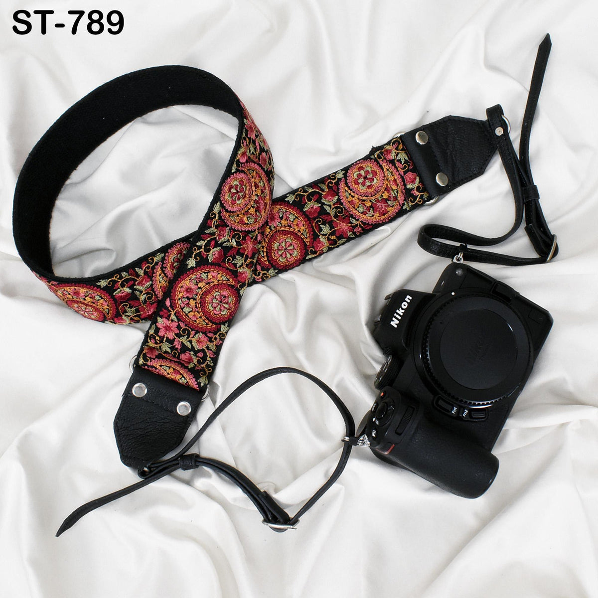 A floral patterned camera strap and a black camera with a lens attached are placed on a white fabric surface.