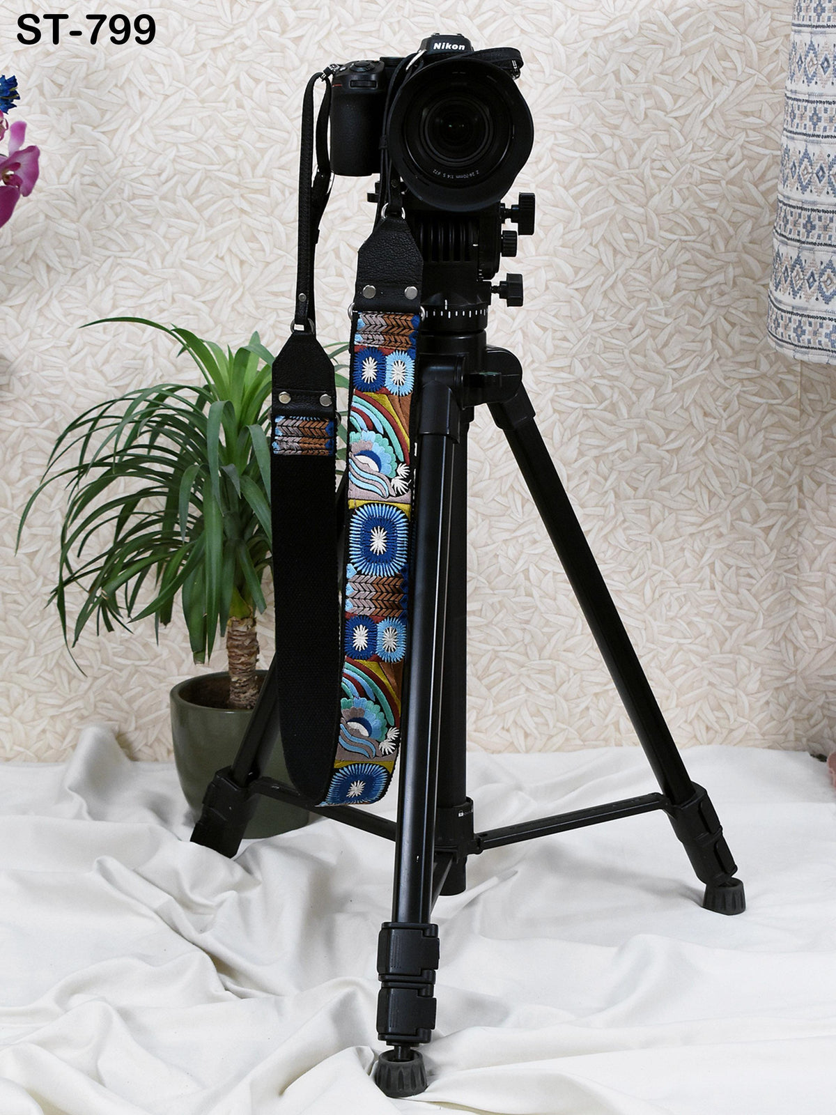 A black tripod with a camera attached to it, standing on a white surface.