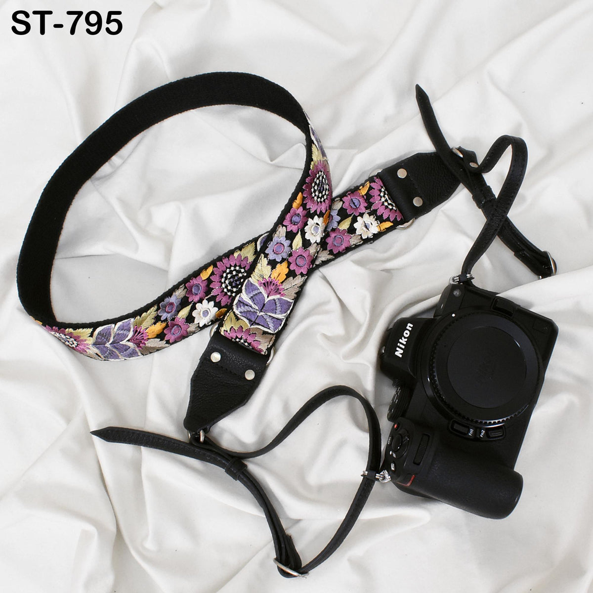 A floral patterned camera strap and a black Nikon camera are placed on a white fabric surface.