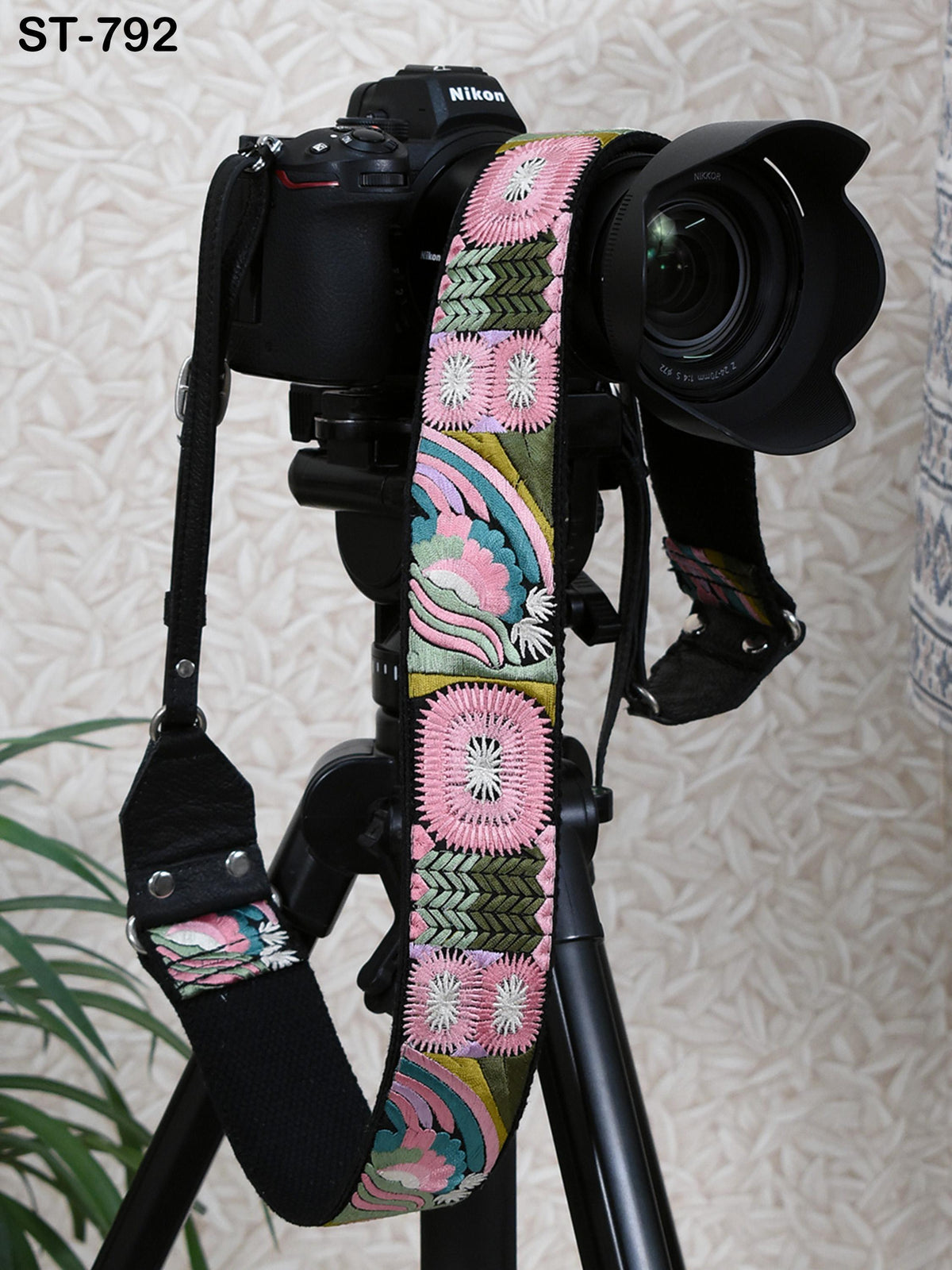 A black camera with a colorful patterned strap attached to it, placed on a tripod against a patterned wall.