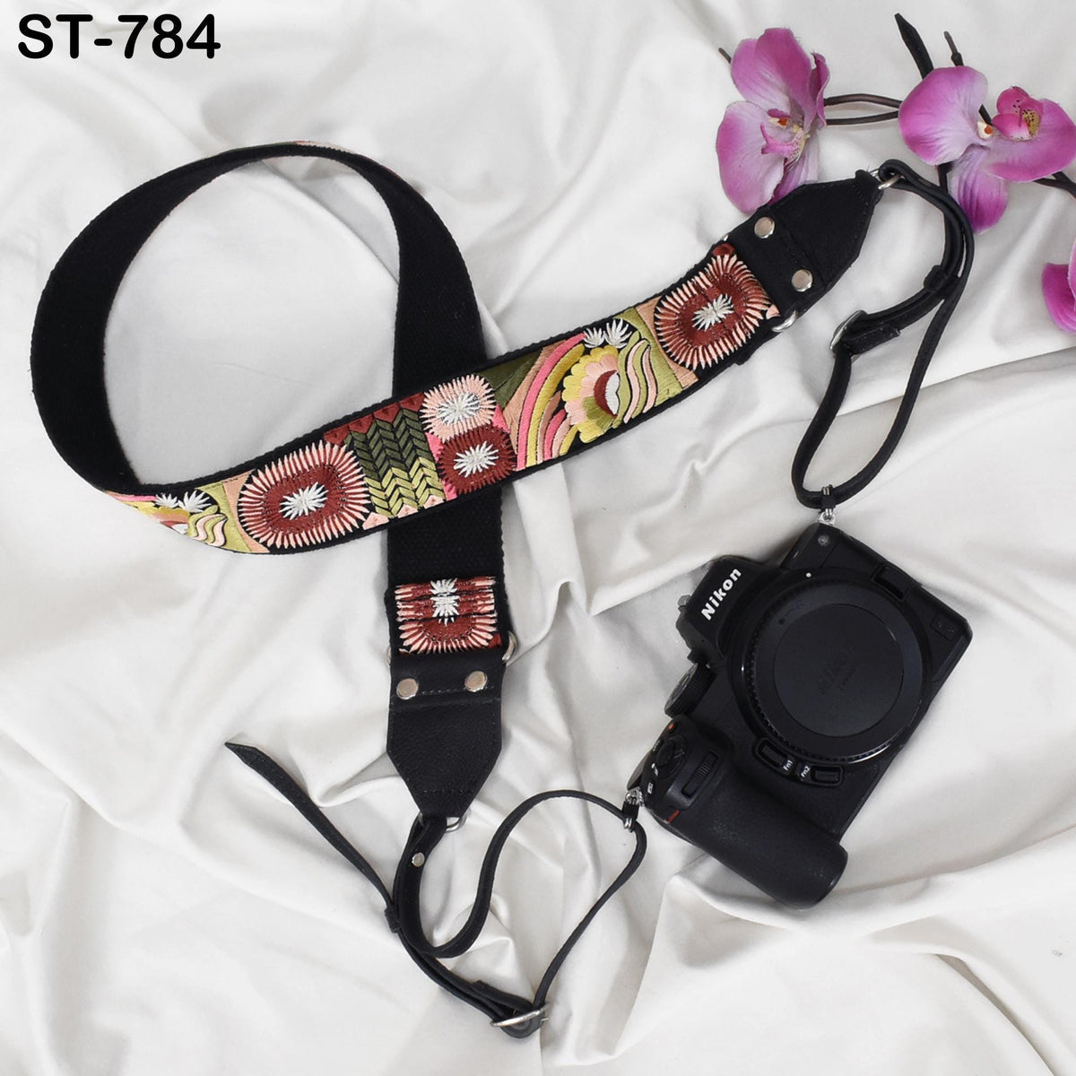 A floral patterned camera strap and a Nikon camera are placed on a white fabric background.