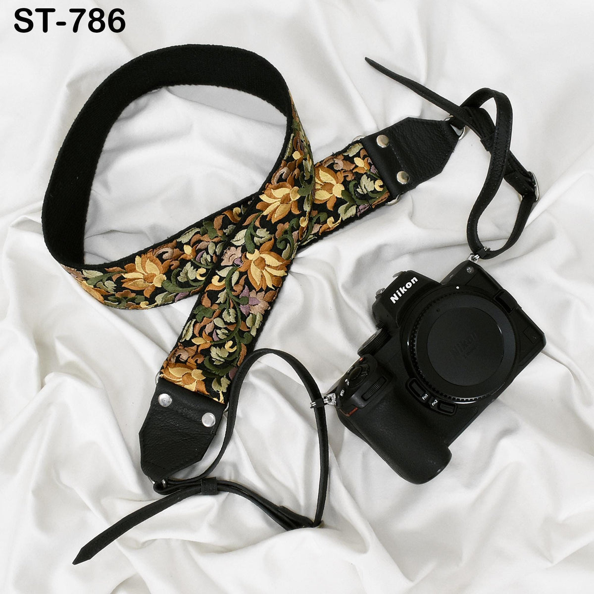 A floral patterned camera strap and a black camera body are placed on a white surface.