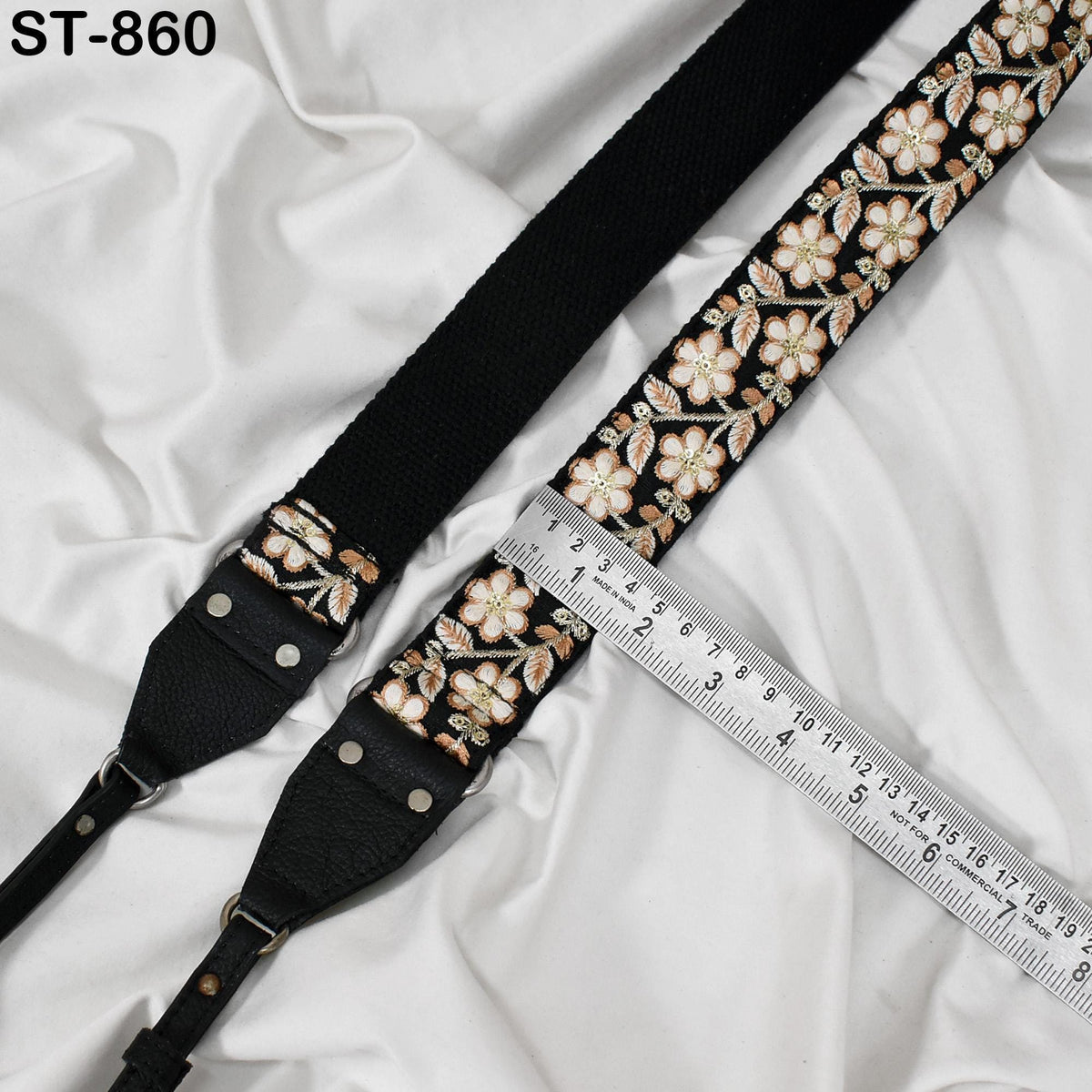 a black strap with a floral pattern and a ruler placed on a white fabric background.