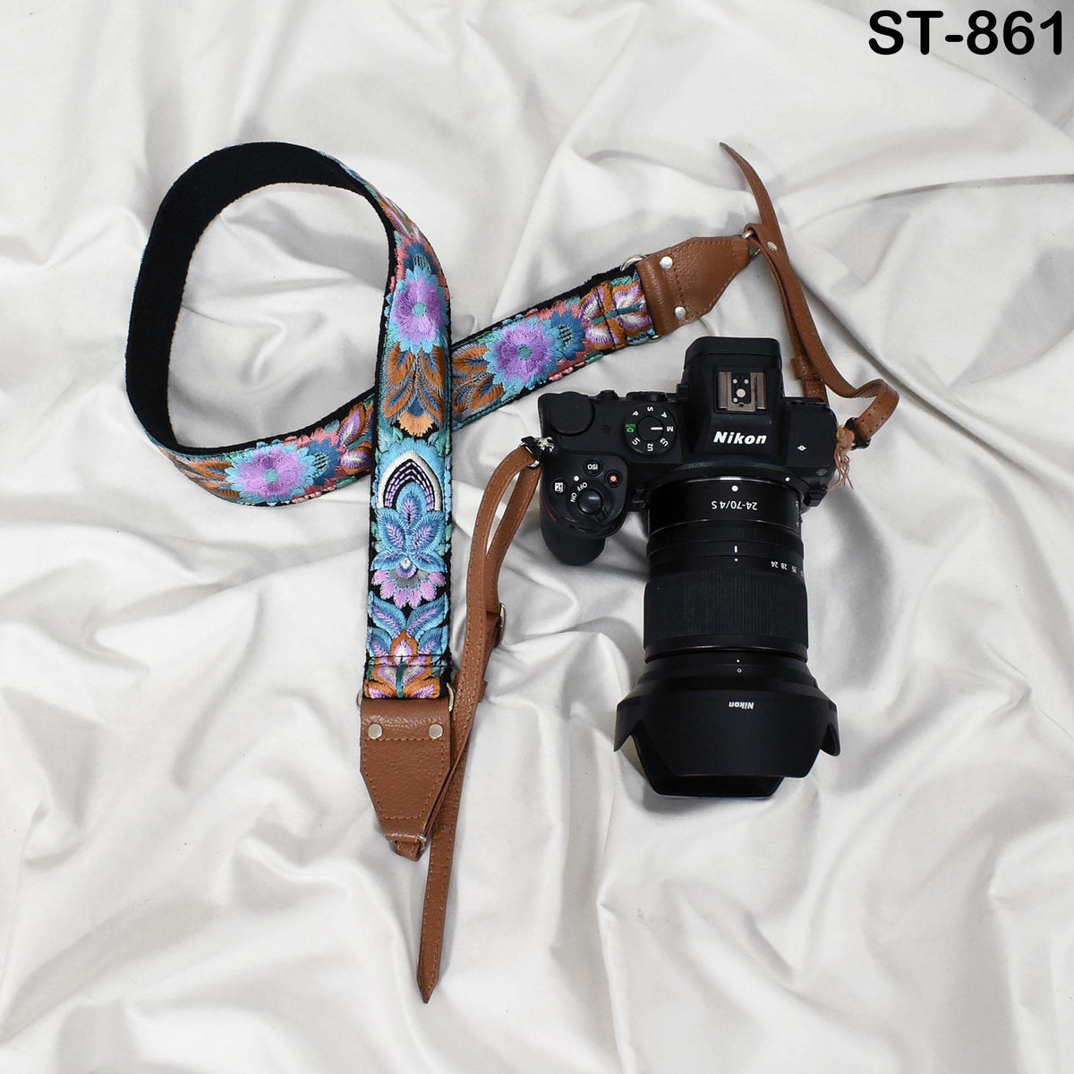 A floral patterned camera strap and a Nikon camera are placed on a white fabric surface.