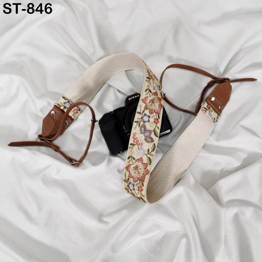 A camera strap with a floral pattern is placed on a white surface, with a camera visible in the background.