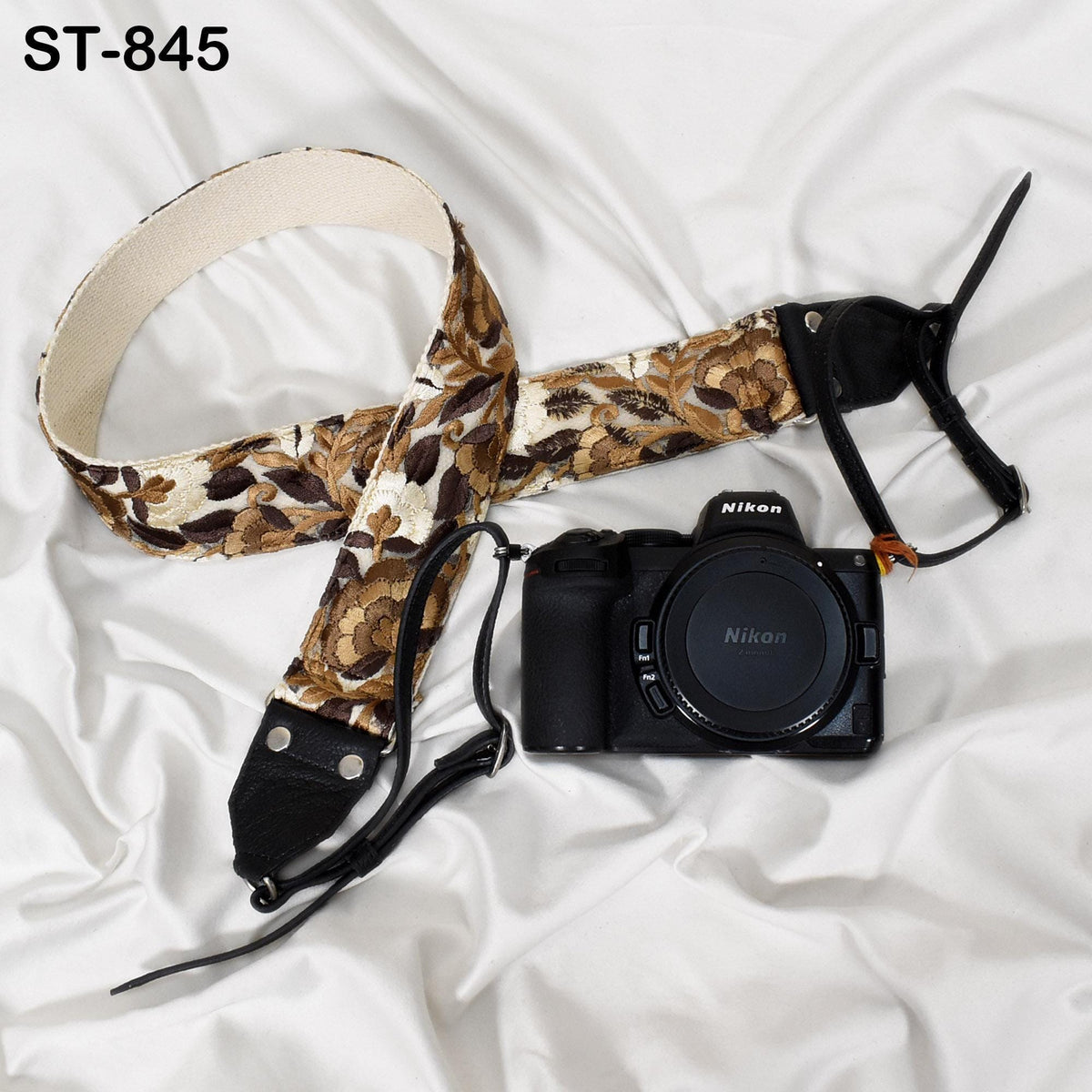 A floral patterned camera strap and a Nikon camera are placed on a white surface.