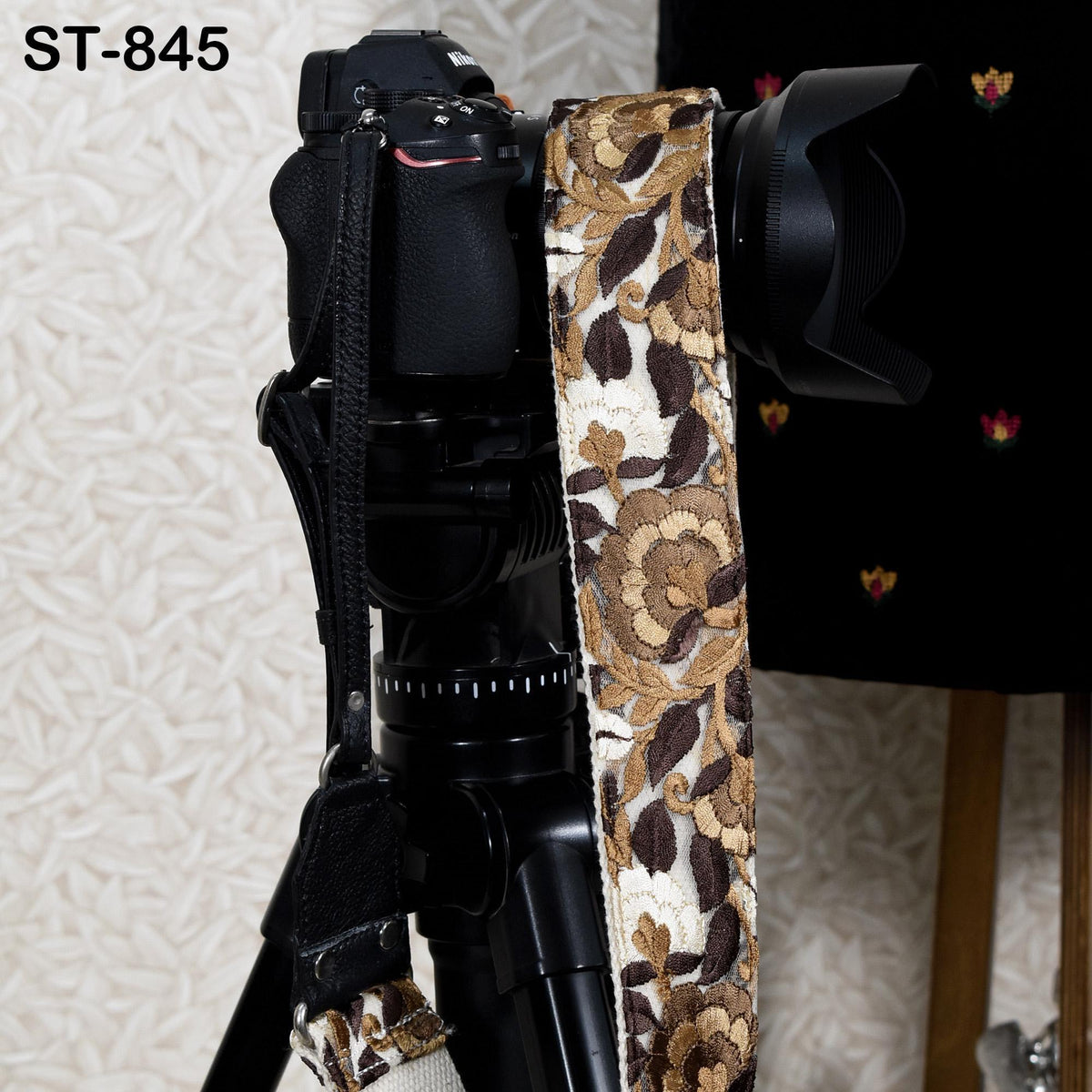 A black camera with a floral patterned strap is mounted on a tripod, with a blurred background.