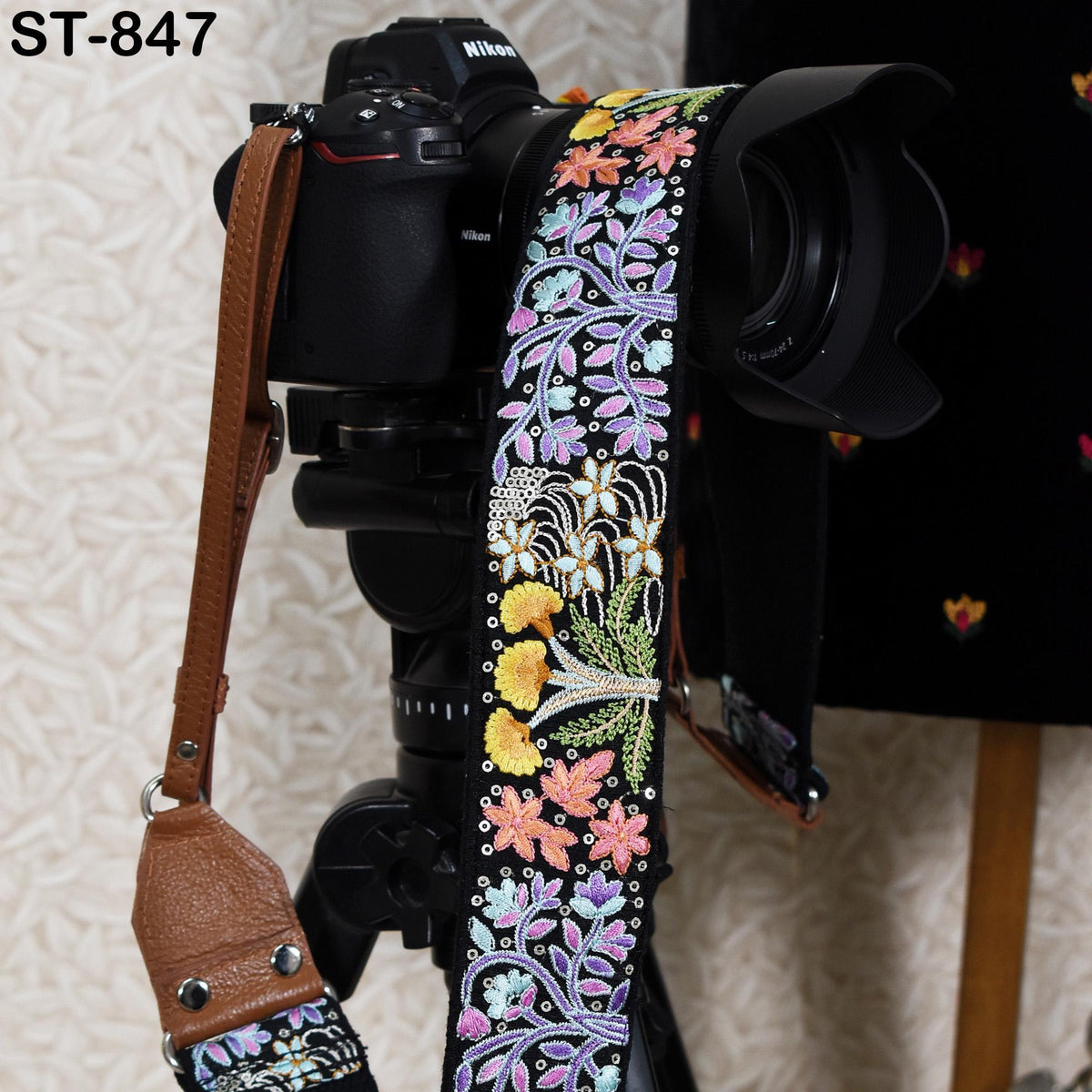 A black camera with a colorful floral patterned strap attached to it, placed on a tripod.