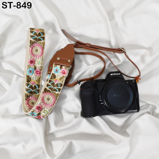 A floral patterned camera strap and a black Nikon camera are placed on a white fabric surface.