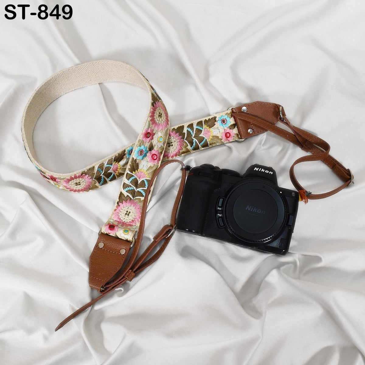 A floral patterned camera strap and a black Nikon camera are placed on a white fabric surface.