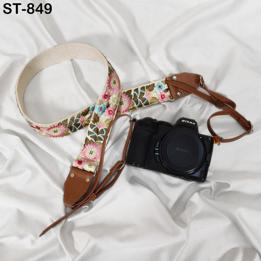 A floral patterned camera strap and a black Nikon camera are placed on a white fabric surface.