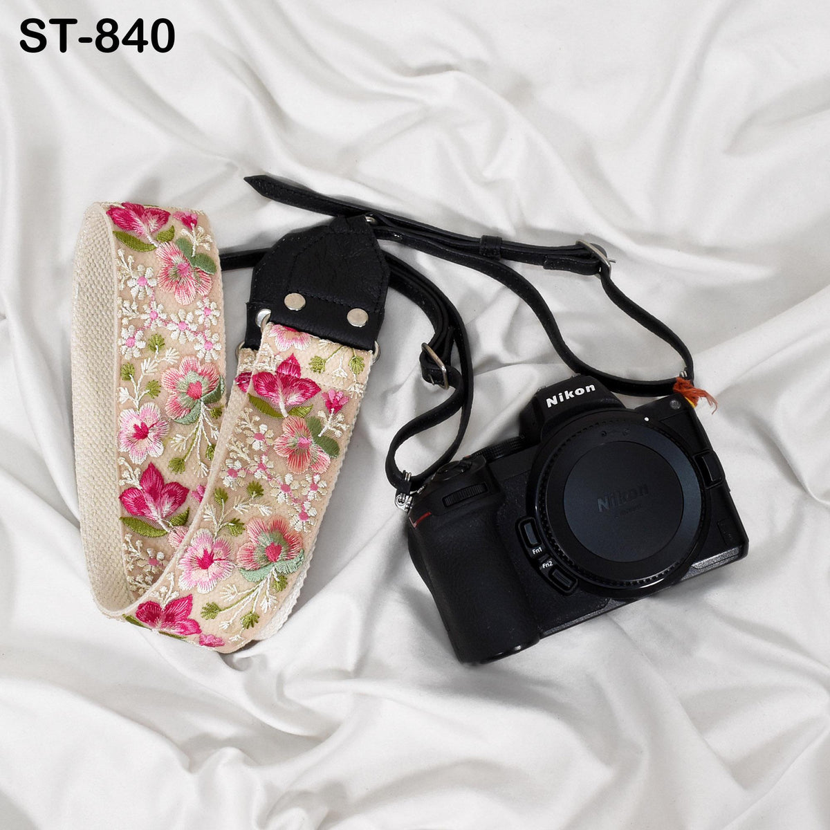 A floral patterned camera strap and a black Nikon camera are placed on a white fabric surface.