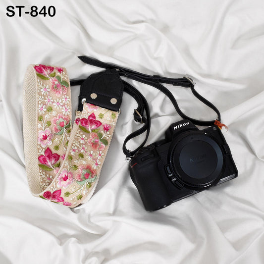 A floral patterned camera strap and a black Nikon camera are placed on a white fabric surface.