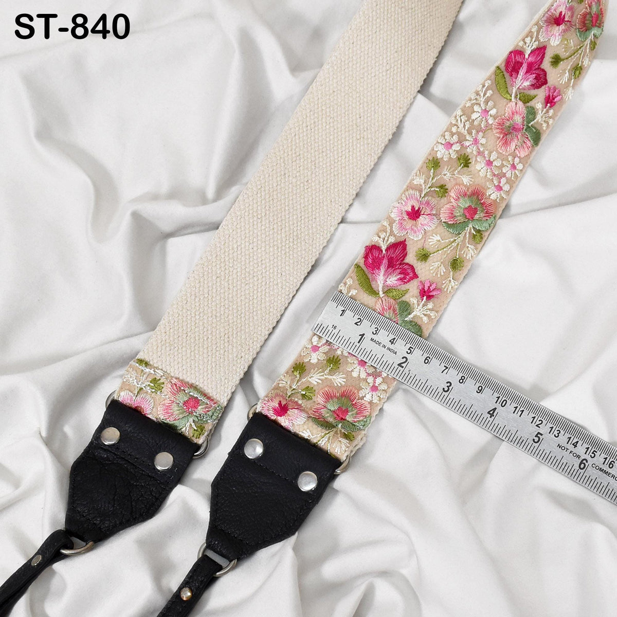 A floral-patterned strap with a black leather buckle, placed on a white fabric surface. A ruler is visible next to the strap, indicating its size.