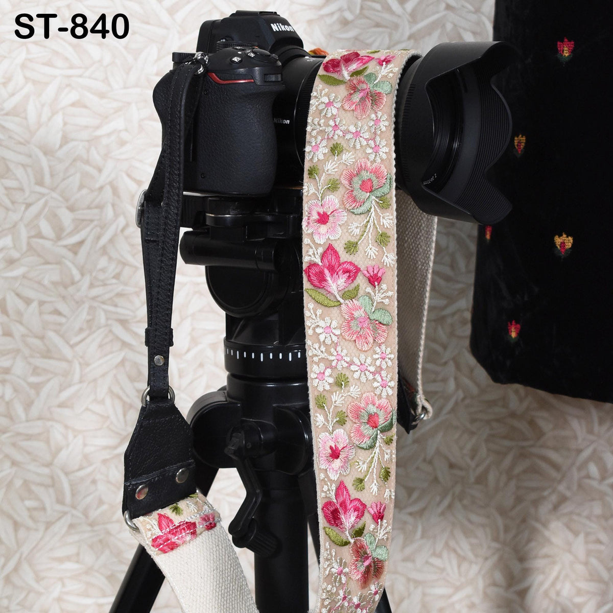 A black camera with a floral patterned strap attached to it, placed on a tripod against a patterned background.