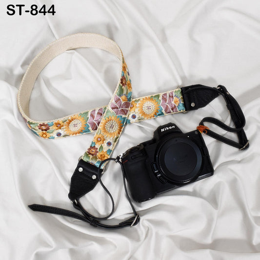A floral patterned camera strap and a black Nikon camera are placed on a white fabric surface.