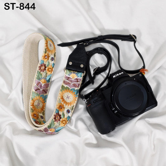 A floral patterned camera strap and a Nikon camera are placed on a white surface.