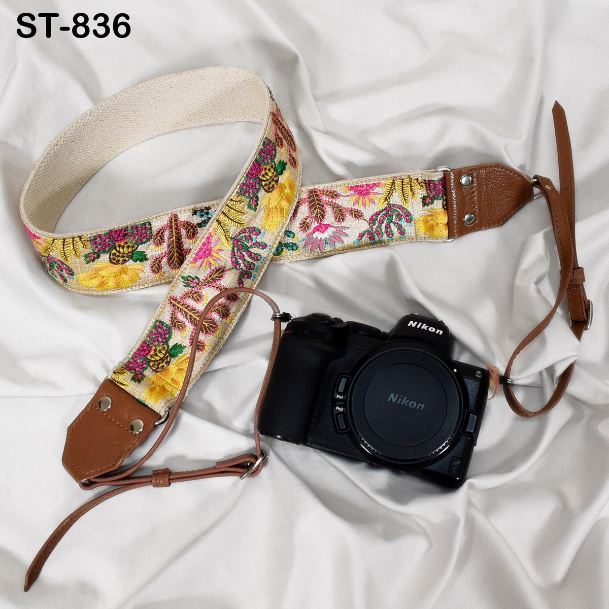A floral patterned camera strap and a Nikon camera are placed on a white fabric surface.