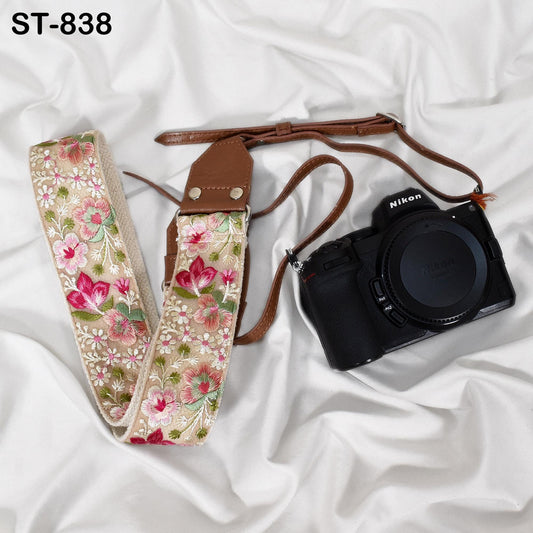 A floral patterned camera strap and a black Nikon camera are placed on a white, crumpled surface.